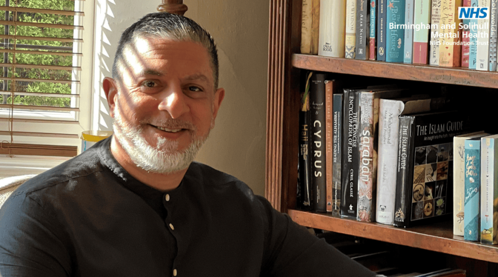 Javid smiling on an armchair near a bookcase